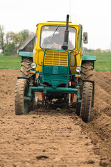 Plowing and sowing the soil with an old farm tractor Belarus in an agricultural field in spring,...