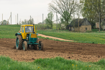 Plowing and sowing the soil with an old farm tractor Belarus in an agricultural field in spring,...