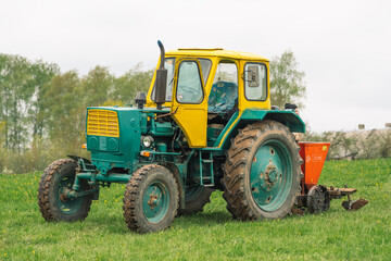 Old farm tractor Belarus on the green grass in an agricultural field in spring ready for the plowing and sowing 