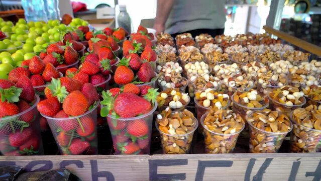 Market is in Georgia, in plastic cups there are dried fruits, nuts, strawberries and cherry plum in winds. Spontaneous market. Table with local delicacies. Camera movement.