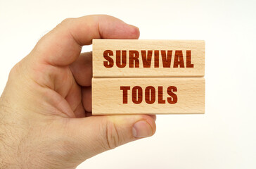 On a white background, a hand that holds wooden blocks with the inscription - Survival Tools