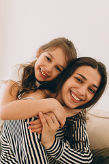 Portrait of little preteen girl hugging her elder sister of 20s in striped clothes, putting hands around neck, showing her love and affection. Family, relatives, siblings concept. Happy childhood