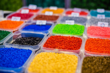 Plastic recycling, renewable resource - heap of colorful secondary polystyrene, polyethylene, polypropylene granules or pellets in containers on table at exhibition, trade show - close up