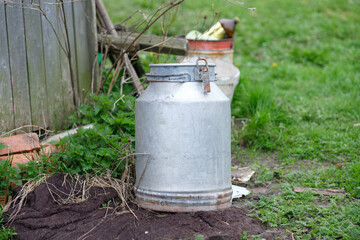 Rural background with an old milk can on the grass near a wooden fence