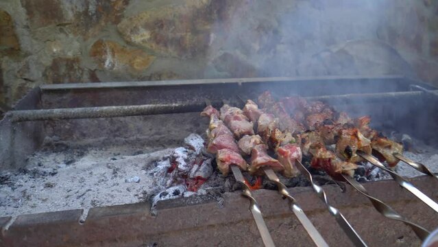 Pickled kebab is grilled on coals. Man's hand stirs skewer. Delicious pieces of marinated meat, strung on skewers, cooked on charcoal grills in fragrant hot smoke.