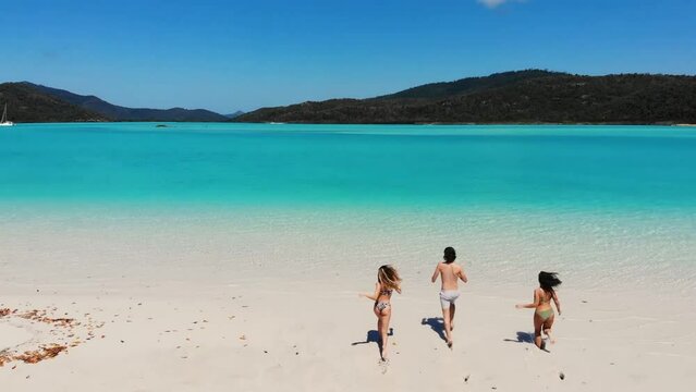 Aerial drone view of friends running into the turquoise water in whitsundays