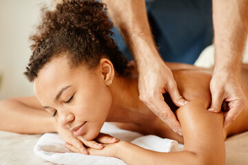 Obraz na płótnie Canvas Close up of young African American woman enjoying back massage in relaxing SPA session and smiling blissfully