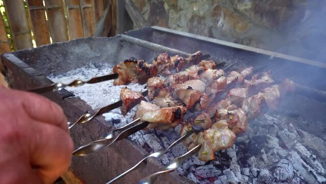 Pickled kebab is grilled on coals. Man's hand stirs skewer. Delicious pieces of marinated meat, strung on skewers, cooked on charcoal grills in fragrant hot smoke.