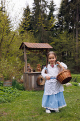 Portrait of ittle 5-eyar-old girl with a basket of bread and buns in park and eating pretzel. Little baby girl of 5-years-old in retro vintage dress having fun and smiling in forest 