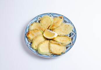 Tasty fried zucchini with lemon on plate, top view, isolated on white background