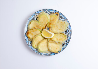Tasty fried zucchini with lemon on plate, top view, isolated on white background