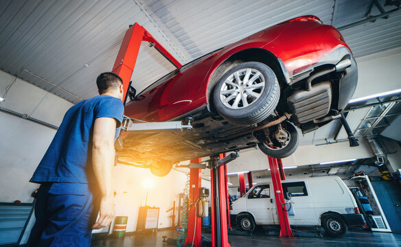 Mechanic lifting modern red car on repair lift. Auto repair station