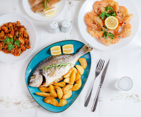 Traditional  Greek food, Dorada fish with Greek salad, Mediterranean traditional menu, Grilled sea bream, shrimps or prawns  zucchini, variety of seafood, mussels, tzatziki, potatoes, feta and ouzo