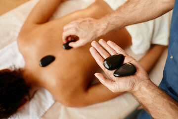 Top view closeup of young man laying stones on back of young woman in relaxing SPA session, copy space