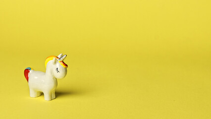 Unicorn little toy on yellow background with copy space. White unicorn with closed eyes. - obrazy, fototapety, plakaty