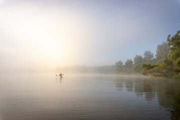 Silhouette of a man in a boat. Mystical landscape. Fog in the early morning on the river. The trees near the water are illuminated by the rays of the rising sun.