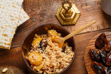 A plate of couscous with saffron and nuts on a wooden table next to matzah and a jug of fruit broth.