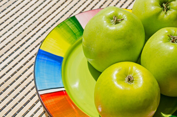 Ripe green apples on a colorful plate.