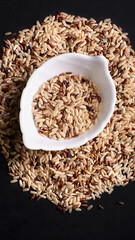 unpolished rice in a saucer and scattered on a black background