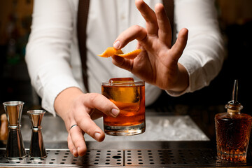 male hand holding glass with alcoholic drink and gently garnishing it with orange zest