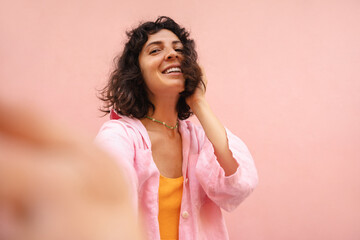 Pretty young brunette caucasian woman takes selfies looking at camera on pink background. Model...