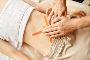 Top down view of rehabilitation therapist putting physio tape on young woman abdomen muscles, copy space
