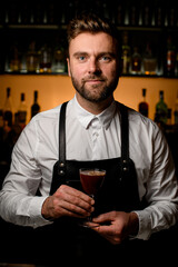 Fototapeta premium handsome male bartender serving alcoholic cocktail in wineglass on the blurred bar background
