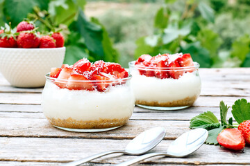 Strawberry desserts with fresh strawberries, cream cheese or natural yoghurt and oat granola in glass jars on wooden table. Delicious healthy organic summer snack or breakfast.