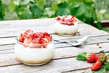 Strawberry desserts with fresh strawberries, cream cheese or natural yoghurt and oat granola in glass jars on wooden table. Delicious healthy organic summer snack or breakfast.