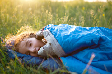 A child sleeps in a sleeping bag on the grass in a camping trip - eco-friendly outdoor recreation,...