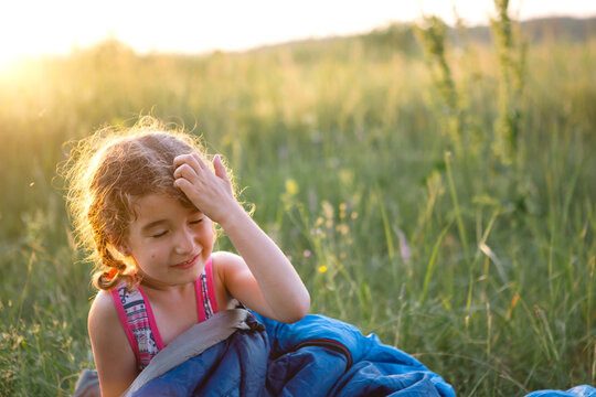 The girl is dissatisfied with scratching mosquito bites, child sleeps in a sleeping bag on the grass in a camping trip. Eco-friendly outdoor recreation, summer time. Sleep disturbance, repellent.