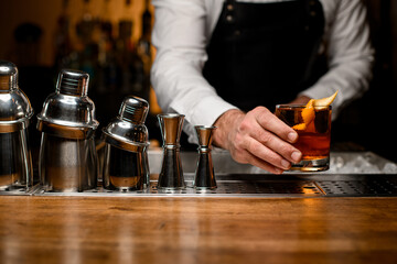 view of row of shakers and male hand holding glass with a drink garnished with orange zest