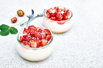 Strawberry desserts with fresh strawberries, cream cheese or natural yoghurt and oat granola in glass jars on light surface top view. Delicious healthy organic summer snack or breakfast