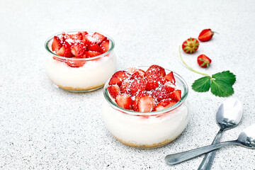 Strawberry desserts with fresh strawberries, cream cheese or natural yoghurt and oat granola in glass jars on light surface top view. Delicious healthy organic summer snack or breakfast