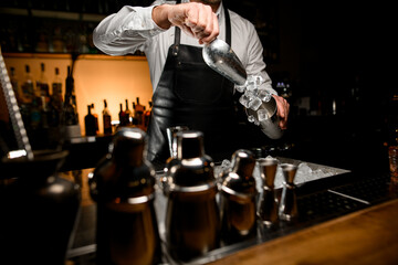 view of ice cubes that bartender pours from scoop into a shaker cup