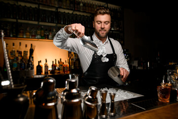 bartender masterfully pours ice cubes from scoop into a shaker cup
