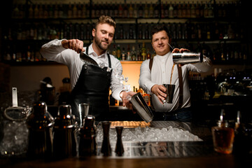 view on two professional bartenders are preparing cocktails in shakers at bar