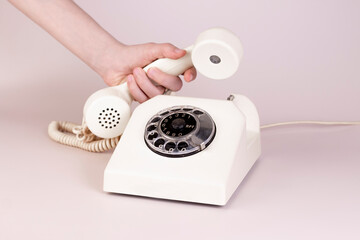Minimal retro concept, girl hand answering vintage phone on light background. Retro telephone call aesthetic, promotion, communication.