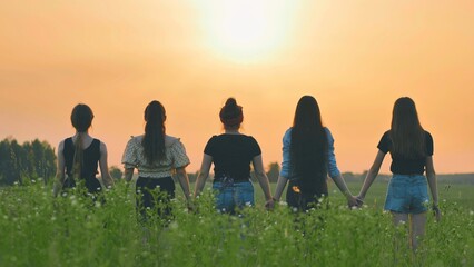 Girls friends waving their hands to the setting sun at sunset.