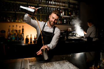 view on cocktail making process where bartender skillfully pours a cocktail in shaker