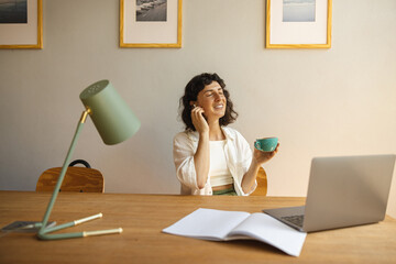 Pretty young caucasian woman is listening to music through headphones sitting at desk with laptop....