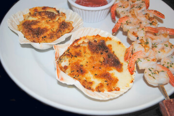 Appetizer of Stuffed Scallop Shells with Cheese and Shrimp and Cocktail Sauce in the Background