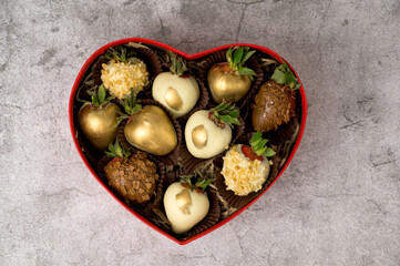Flat lay. Heart shaped box with assorted chocolate covered strawberries on a gray background