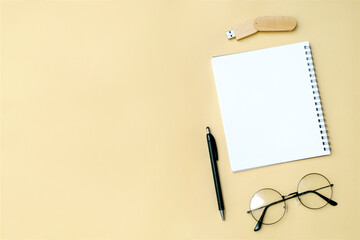 Black blank notebook, pen, glasses, goggles, flash drive top view on beige background. Top view desk arrangement. Time management, planning concept. Minimal style, mock up with copy space