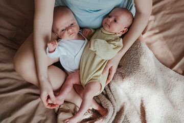 mother holding two twin babies in bed at home
