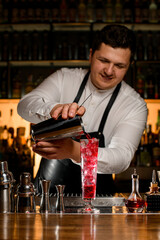 bartender masterfully pours a cocktail from shaker into transparent high glass.