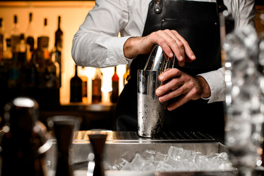 selective focus on shiny steel shaker on the bar counte, which is held by the hands of a male bartender
