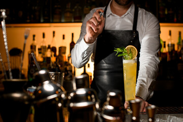 amazing view of tall glass with drink on the bar counter and a male bartender splashes on it