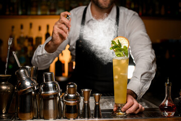 beautiful view of tall glass with drink on the bar counter and bartender carefully splashes on it