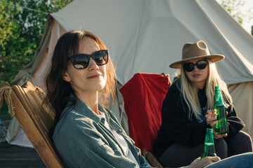 Women friends spending time at the camping in the sun, talk and drink beer